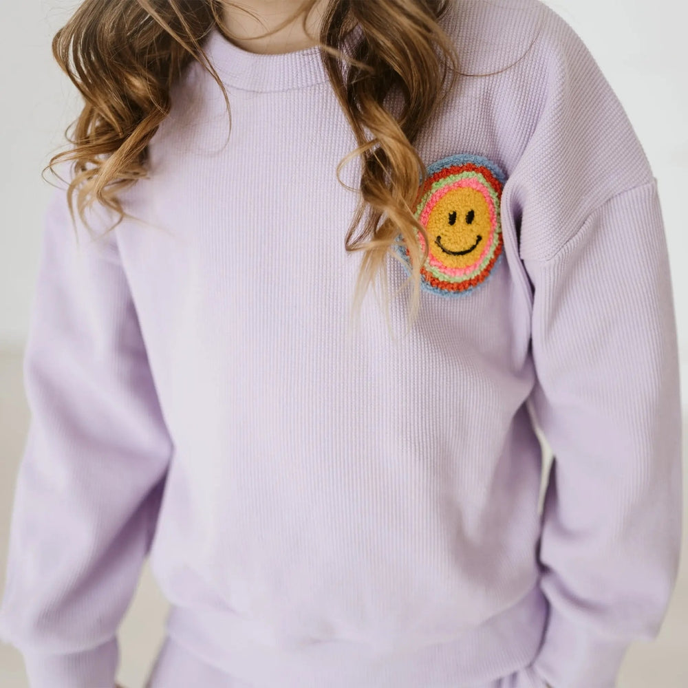 Petite Hailey Waffle Multi Smile Set Purple sweater worn by a girl, lavender knit with a rainbow crochet smile patch.