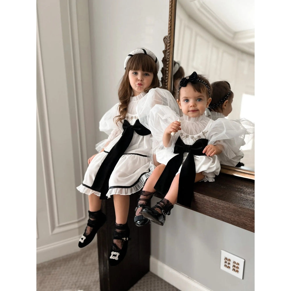 Petite Maison Kids Aurora Ivory Velour Romper on two girls in white puff-sleeve outfits with black sashes, posed on a mantel.