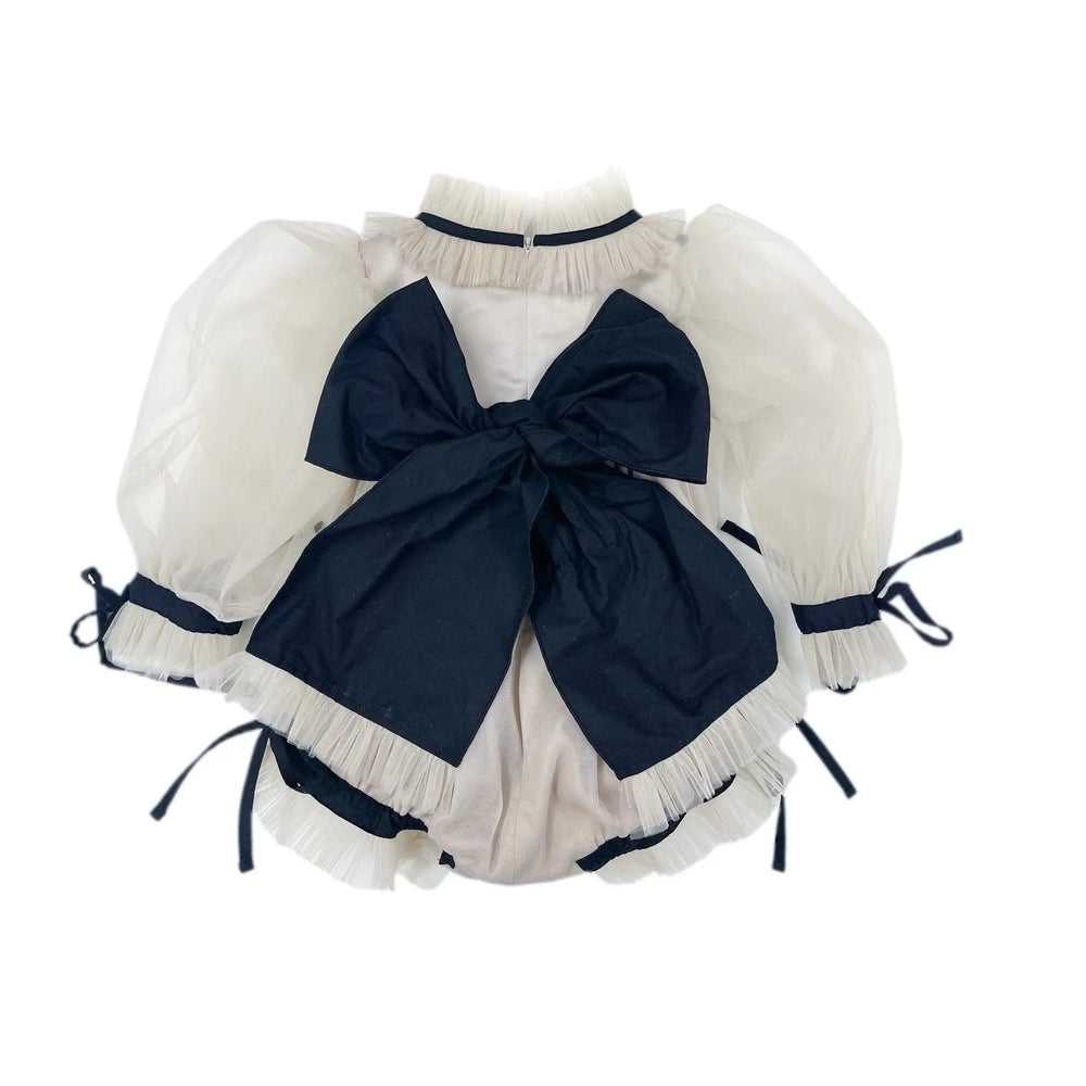 Petite Maison Kids Coco Caramel romper in ivory with sheer puff sleeves and a large navy bow tied at the back.