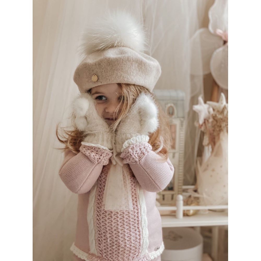 Petite Maison Kids cream wool beret with fluffy pom, pictured on a child in pink knitwear and white mittens.