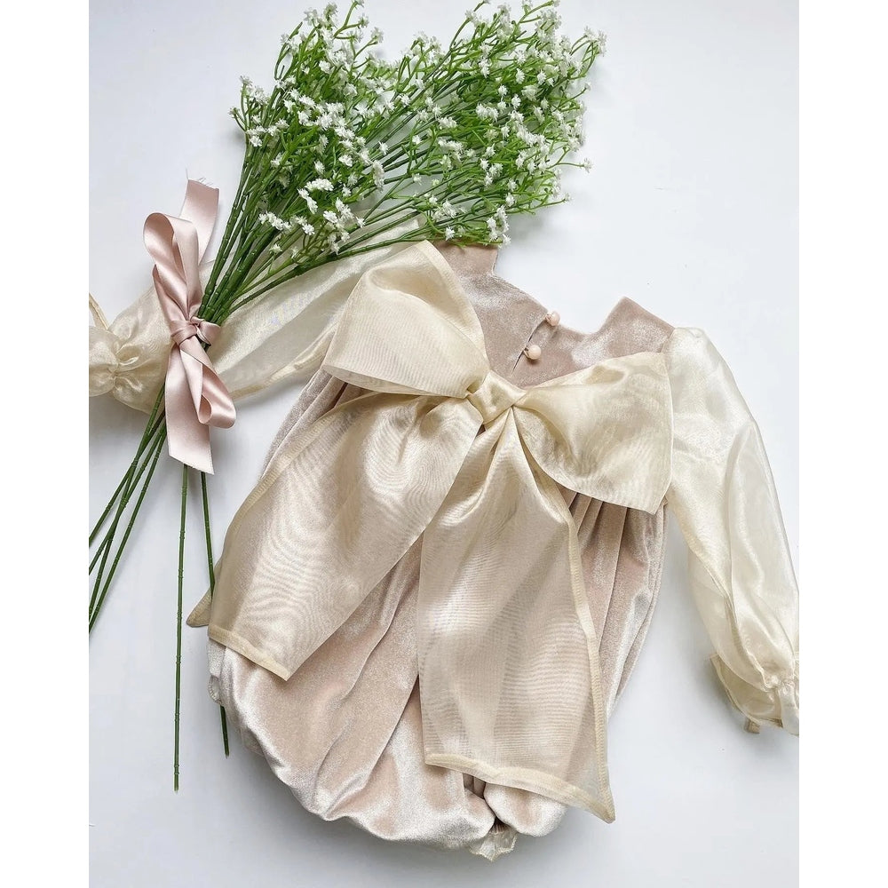 Petite Maison Kids Helena Velour Romper in beige, large satin bow and sheer overlay shown on a flat lay beside flowers.