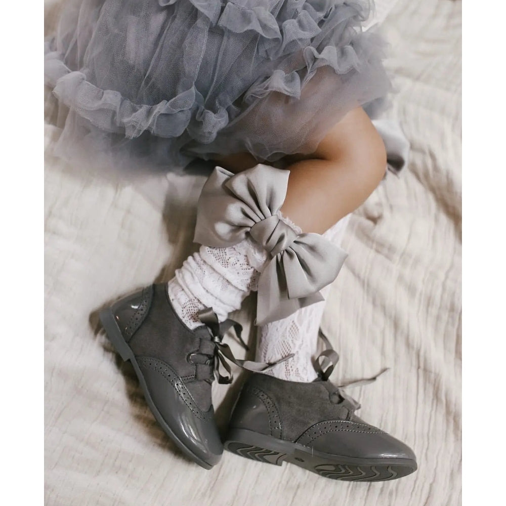 Petite Maison Kids Lola Lace Socks With Satin Bows in gray, featuring a large ankle bow, worn with white lace tights and gray shoes.