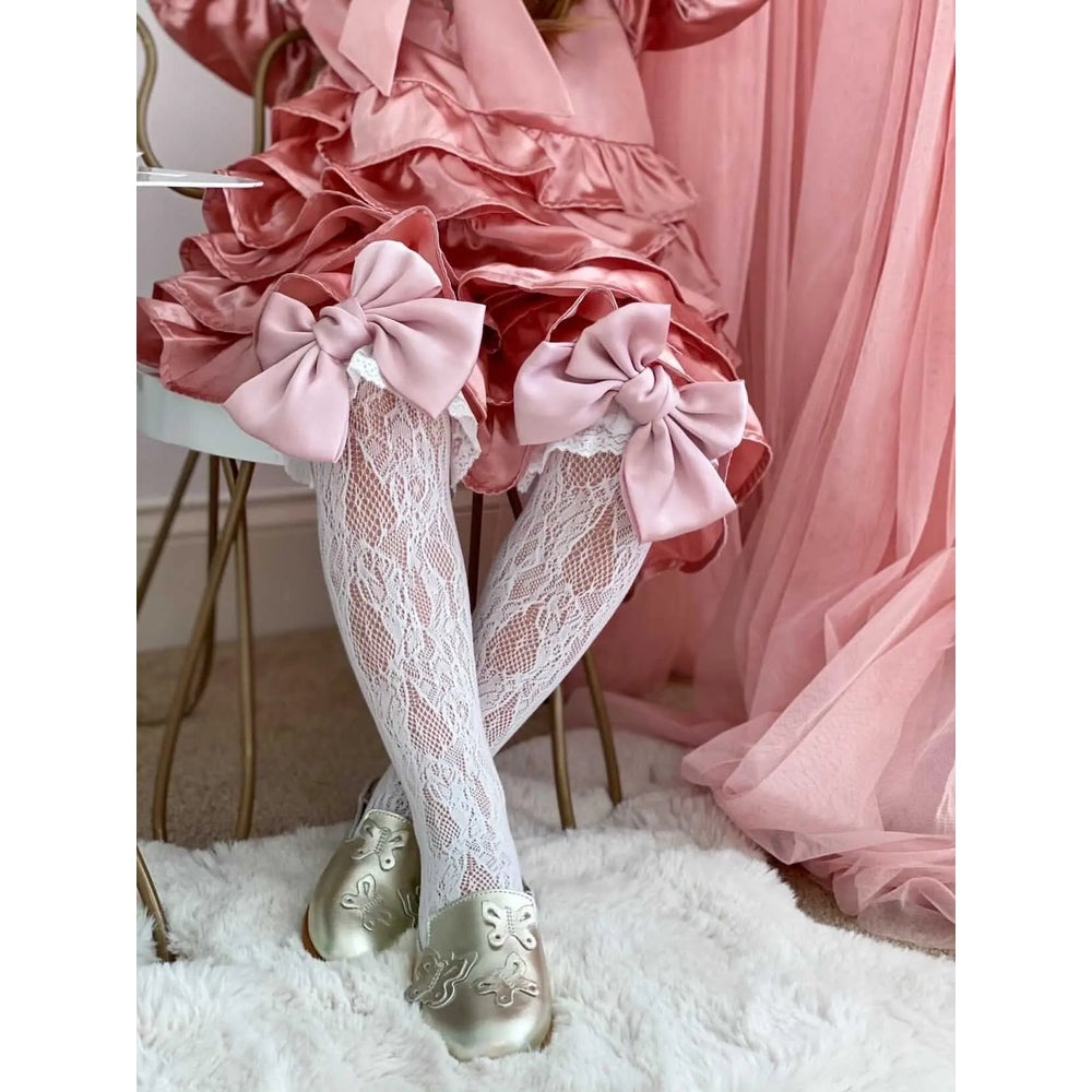 Petite Maison Kids Lola Lace Socks With Satin Bows, white lace socks tied with blush satin bows atop a ruffled pink dress.