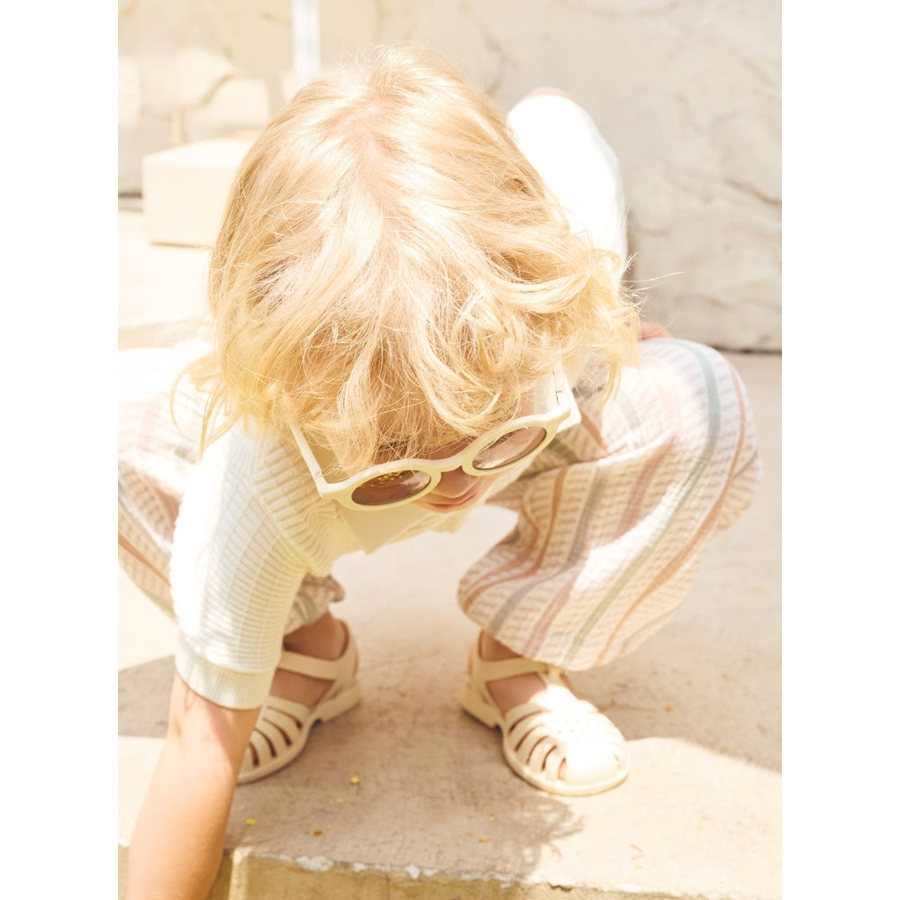 Child wearing sunglasses and a dress, crouching on a stone surface.