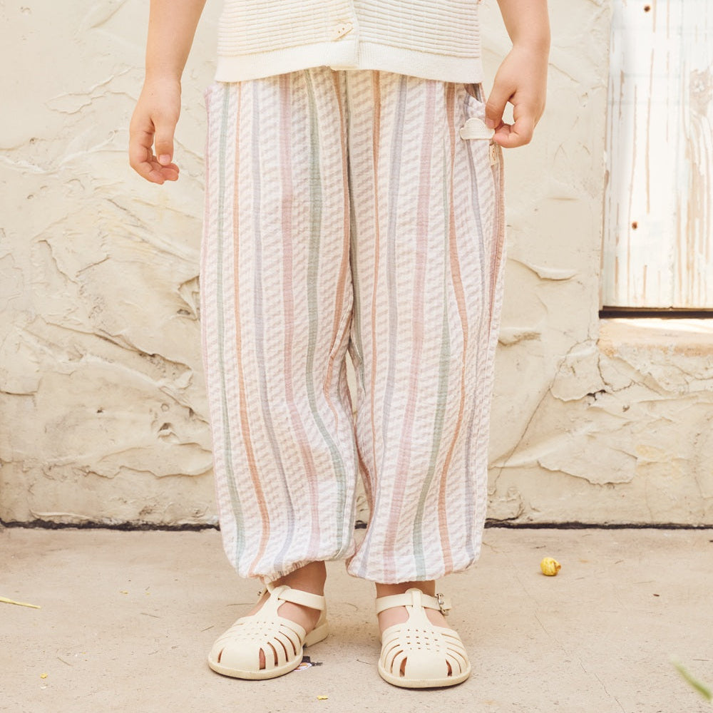 Person wearing a light-colored outfit with striped pants against a textured wall.