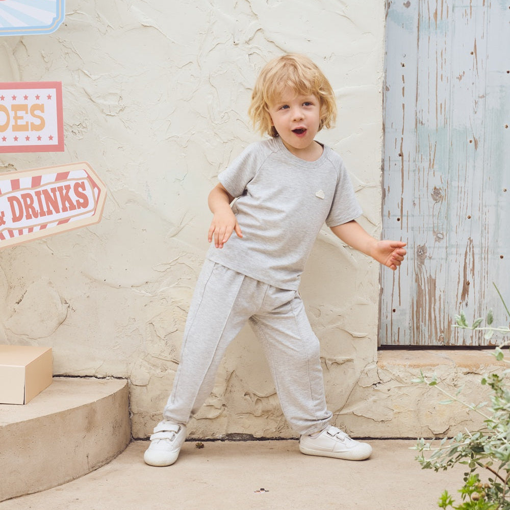 Child in gray outfit standing in front of a textured wall with signs.