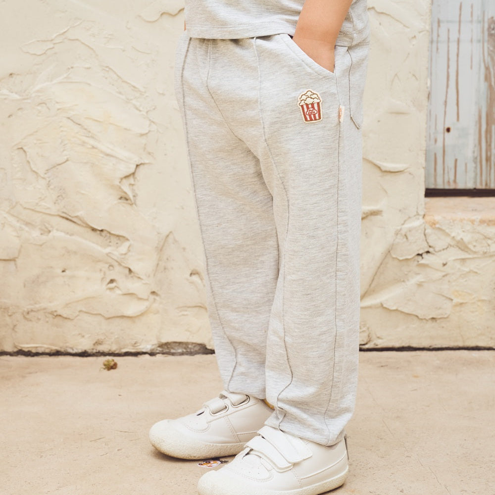 Person wearing light gray sweatpants with a logo and white sneakers on a textured wall background