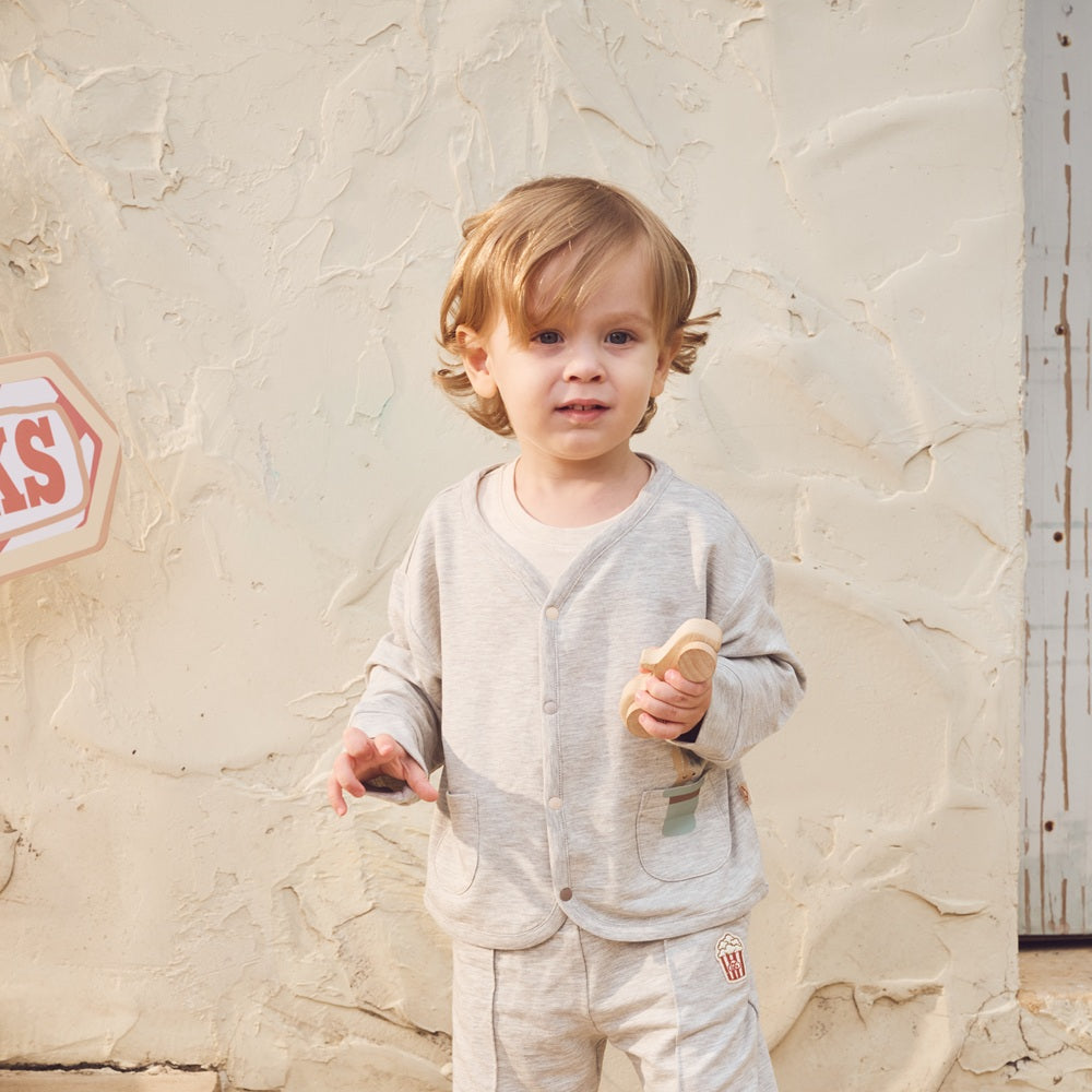 Child wearing a light gray outfit standing against a textured beige wall.