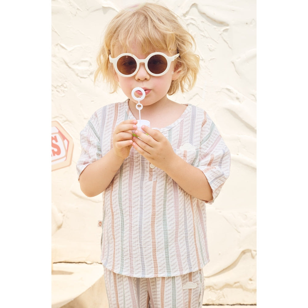 Child blowing bubbles wearing sunglasses and a striped outfit on a white background
