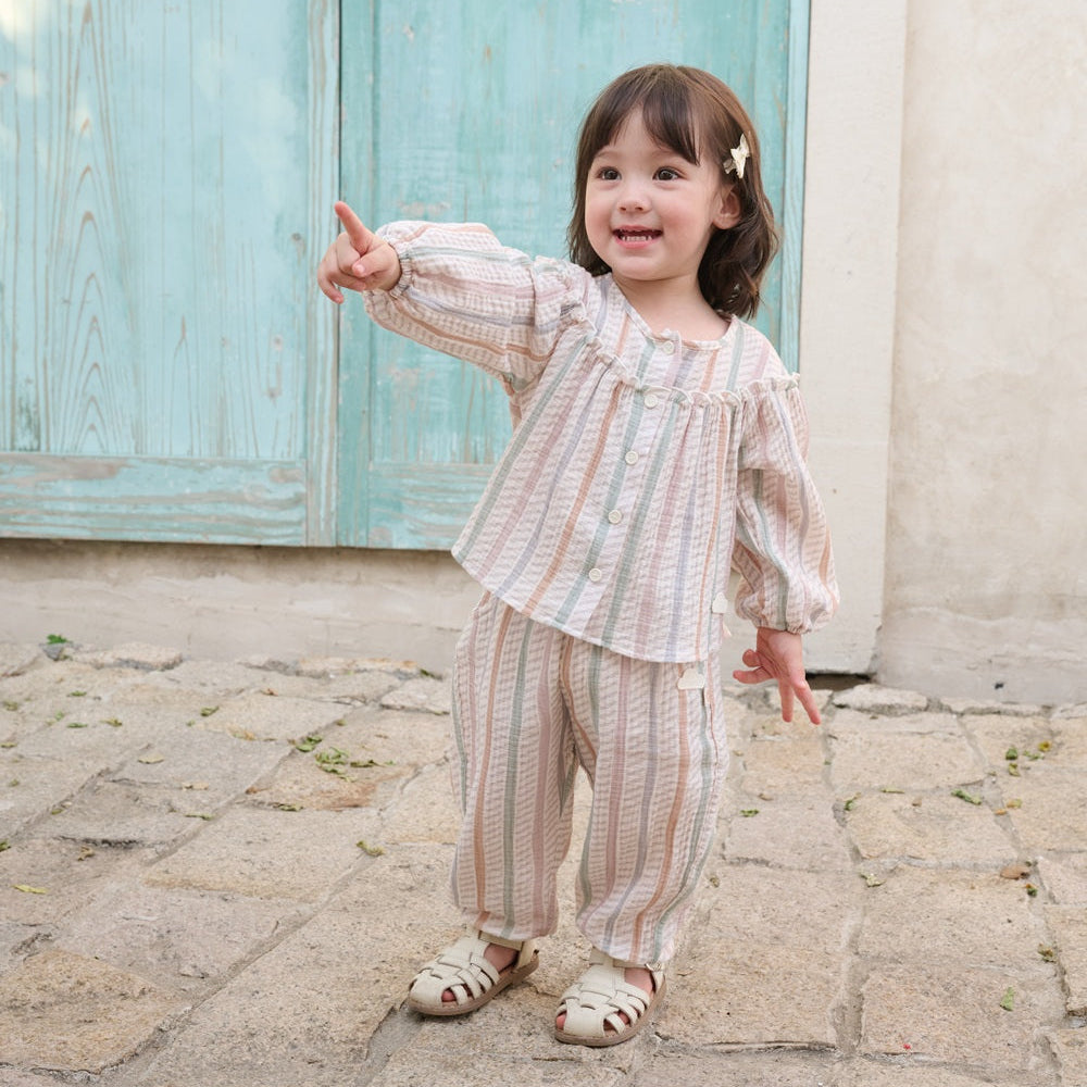 Child in a striped outfit standing on a stone path with a light blue door in the background