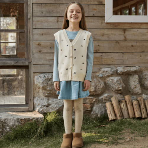 PETITE REVERY cotton knit vest worn by toddler girl, cream color over blue dress with beige tights and tan boots.