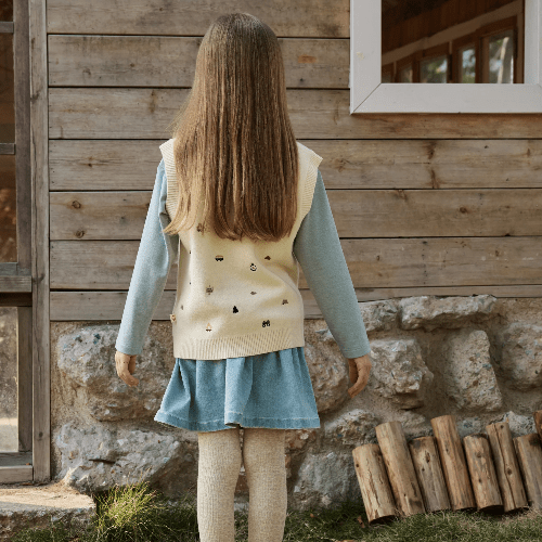 Petite Revery knit vest on toddler girl; cream sleeveless vest over light blue long-sleeve top and blue denim skirt