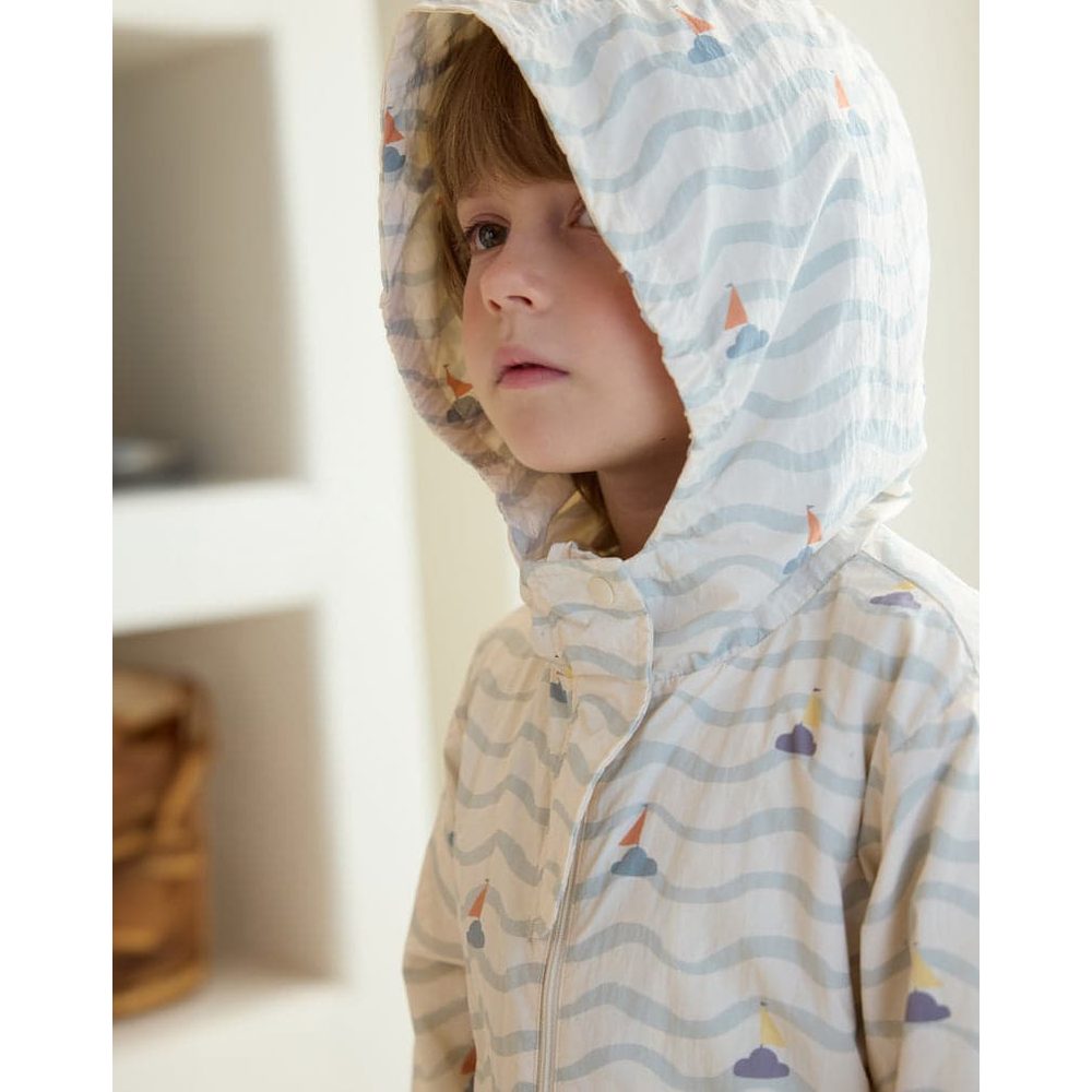 Petite Revery Hooded Windbreaker Sea La Vie; light blue wave pattern with sailboats, worn by a toddler indoors.