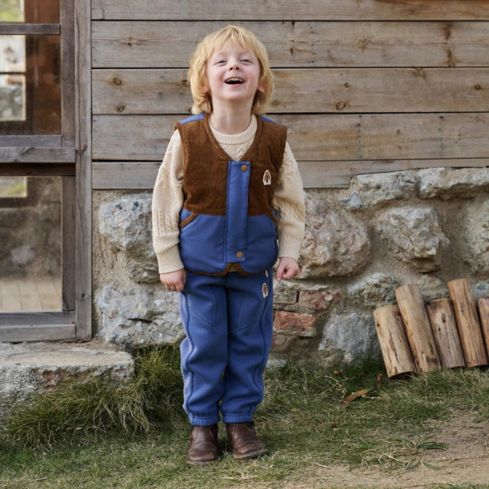 Petite Revery down vest in deep sea blue with brown panels, worn by a smiling child