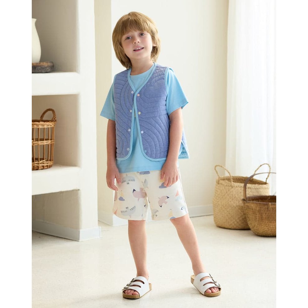 Petite Revery Quilted Cloud Vest Forget-Me-Not worn by toddler, a light blue quilted sleeveless vest over pastel shorts.
