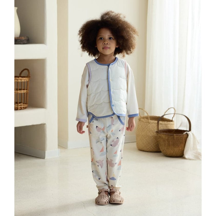 Petite Revery Quilted Sea Vest Jet Stream worn by a toddler standing indoors in pastel printed pajamas with blue trim.