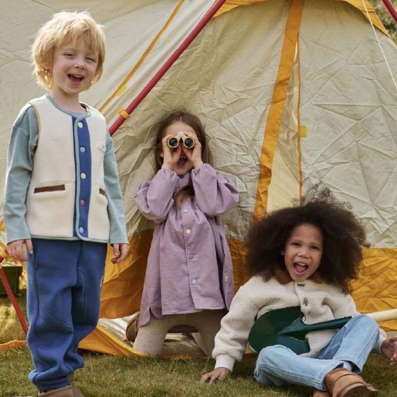Petite Revery recycled fleece vest Cloud for toddlers, cream with blue trim, worn by kids in front of a tent.