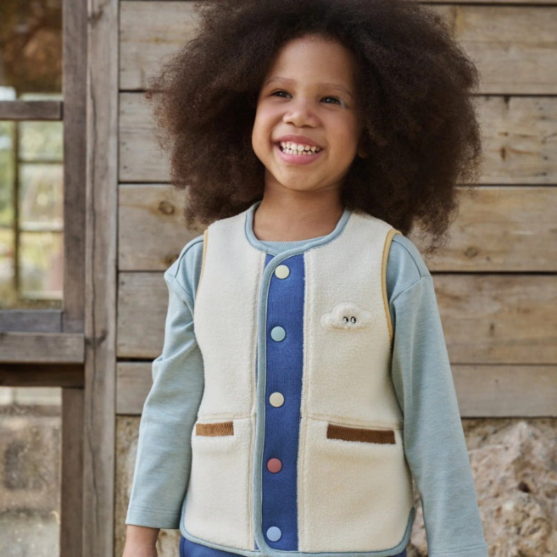 Petite Revery fleece vest, cream with blue center panel and cloud patch on a smiling toddler.