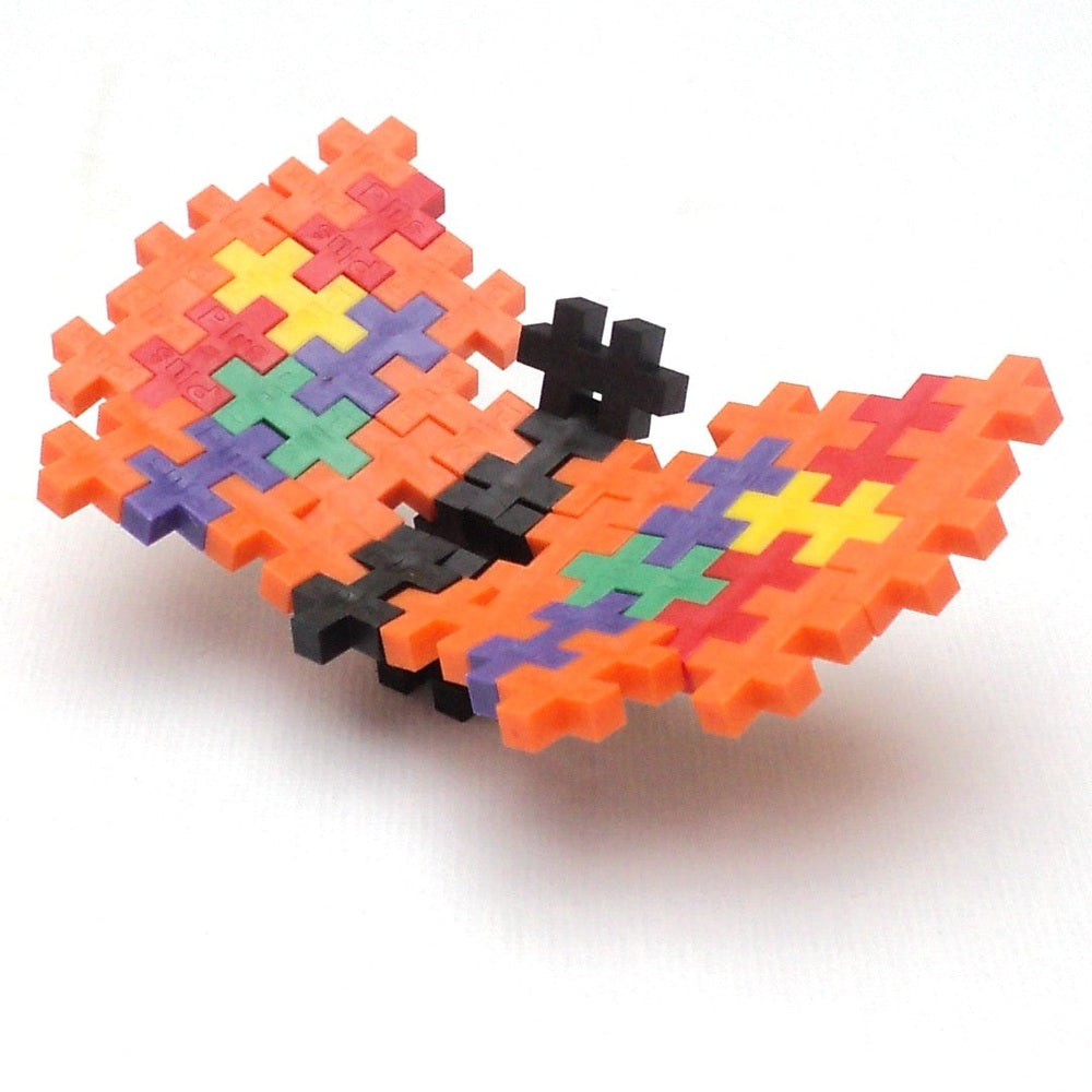 Plus-Plus Mini 3600 Educational butterfly built from orange interlocking pieces with a multicolor center in mid-flight.