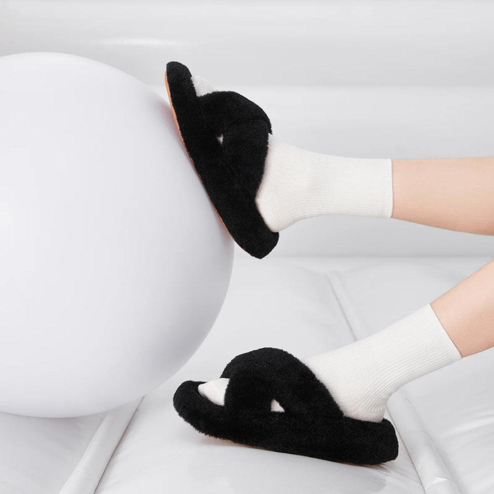 POSEE Cross Strap Plush Fashion Slippers Black worn on white-socked feet, pressing a large white ball.