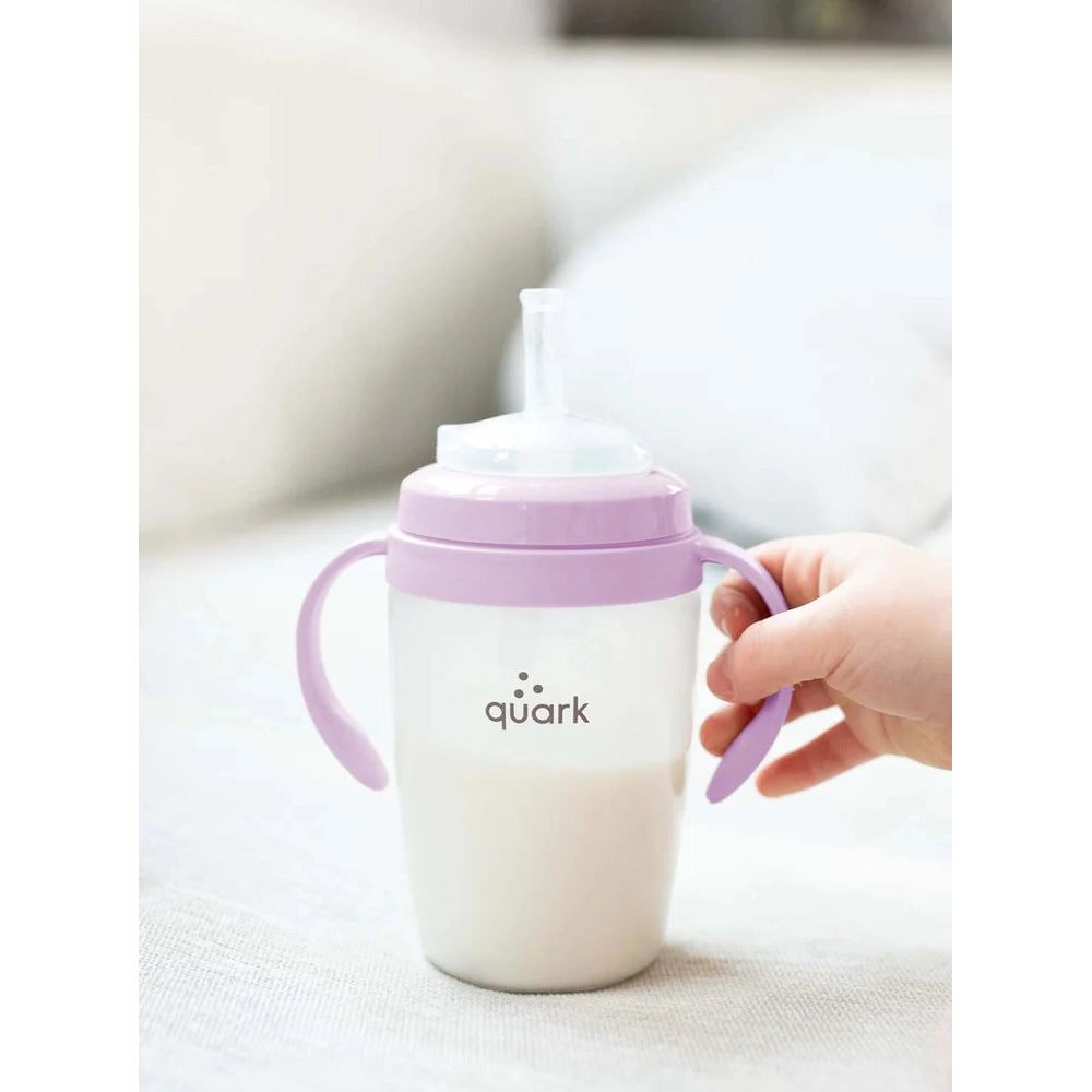 Quark Buubibottle Hybrid Feeding Bundle baby bottle with lavender lid and handles, held by a small hand.