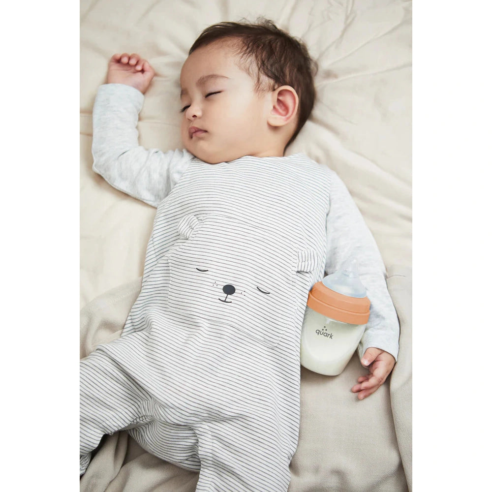 Quark Buubibottle Mini Hybrid Feeding Bottle 1 Pack beside asleep baby, orange lid visible.