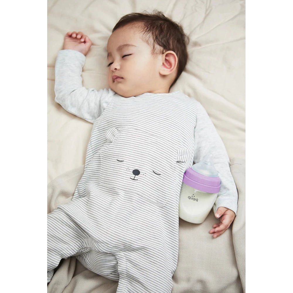 Sleeping baby beside a Quark Buubibottle Mini Hybrid Feeding Bottle 2 Pack with purple lid.