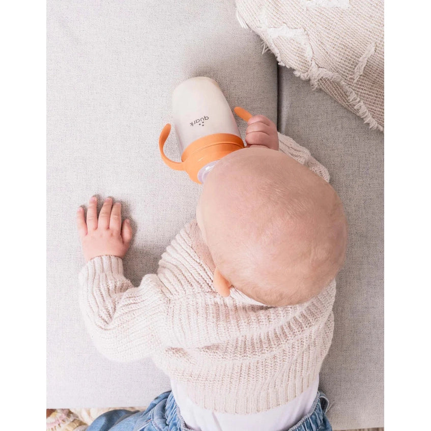 Quark Buubibottle Sipkit training cup conversion kit with orange handles, attached to a baby bottle being used by a baby.