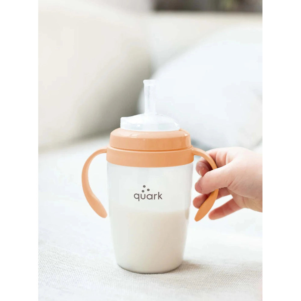 Quark Buubibottle Sipkit Training Cup Conversion Kit in peach lid with dual handles, held for easy one-handed sipping.