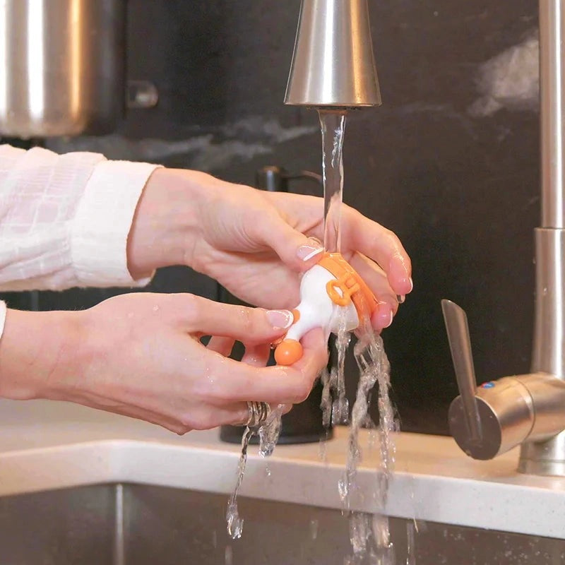 Quark Fruuti baby fruit feeder pacifier, orange and white silicone, being rinsed under running water