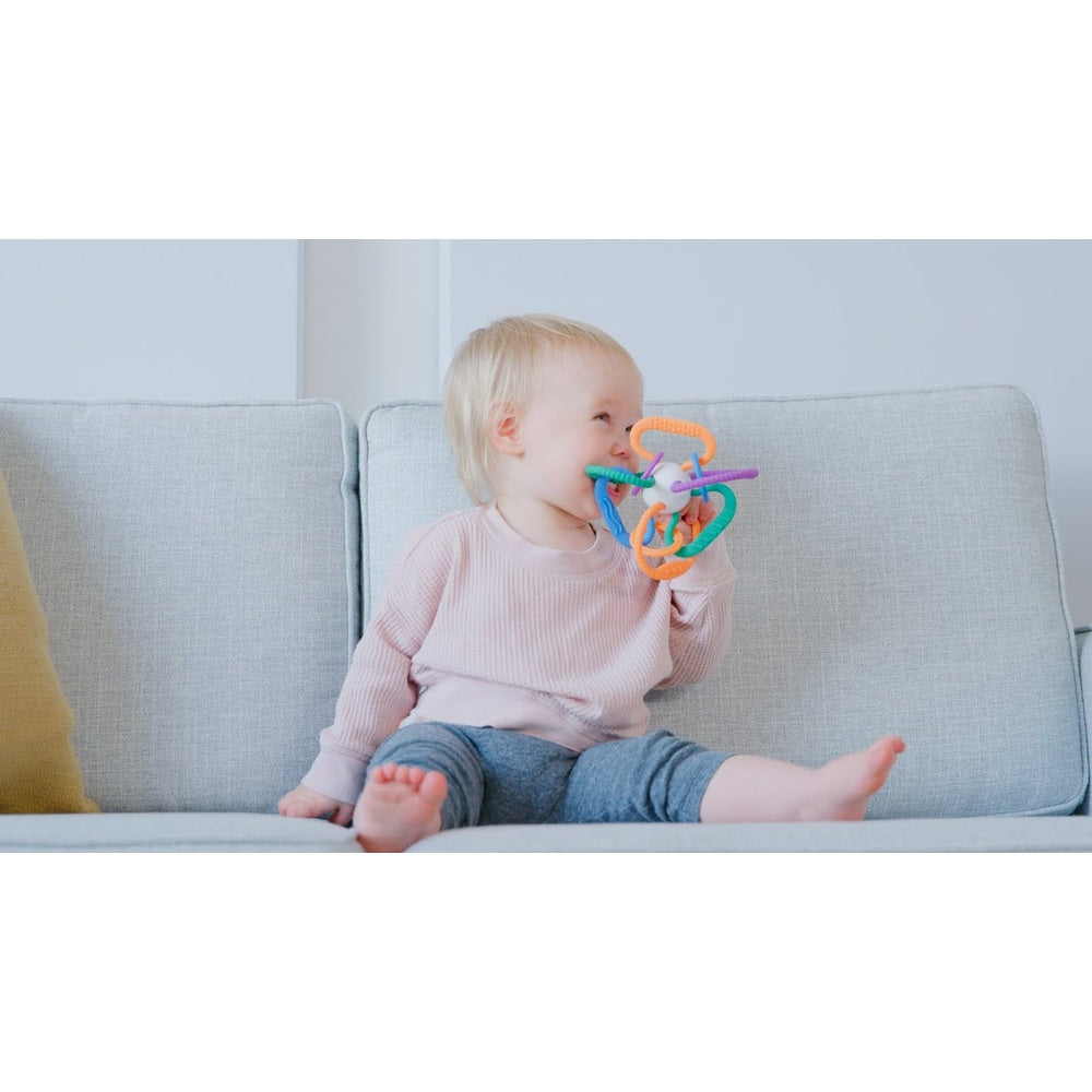 Quark Thiingy sensory teething ball held by baby on gray sofa; colorful silicone teether