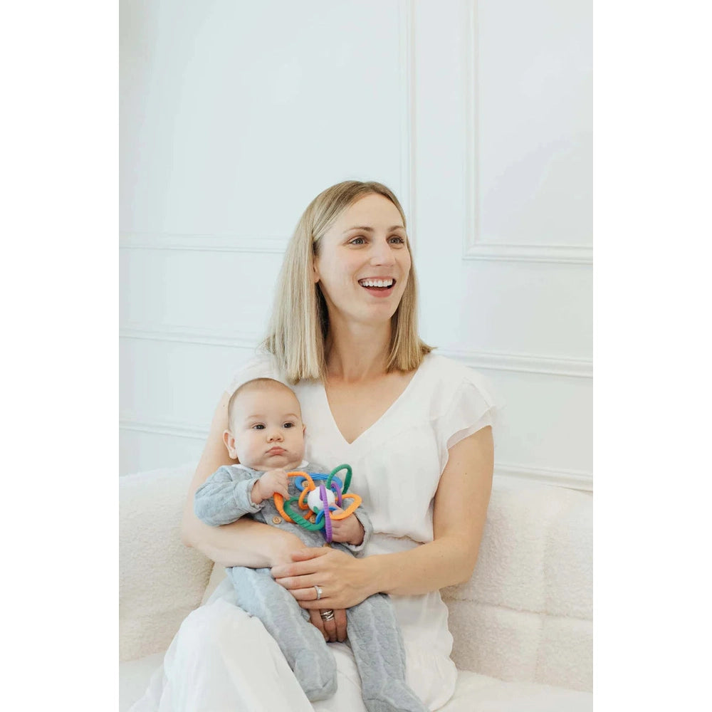 Quark Thiingy sensory teething ball with colorful rings held by a smiling mom and baby