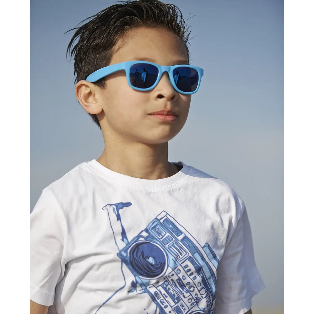 Real Shades Surf Sunglasses Kids Neon Blue worn by a boy with blue mirrored lenses reflecting the sky
