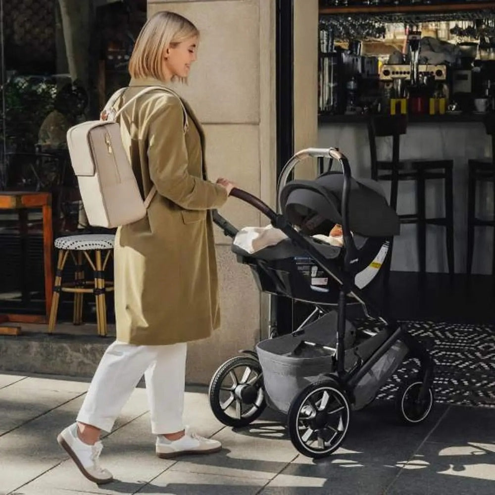 ROMER Juni Infant Car Seat with Versa Base attached to a stroller, being pushed by a woman outdoors.