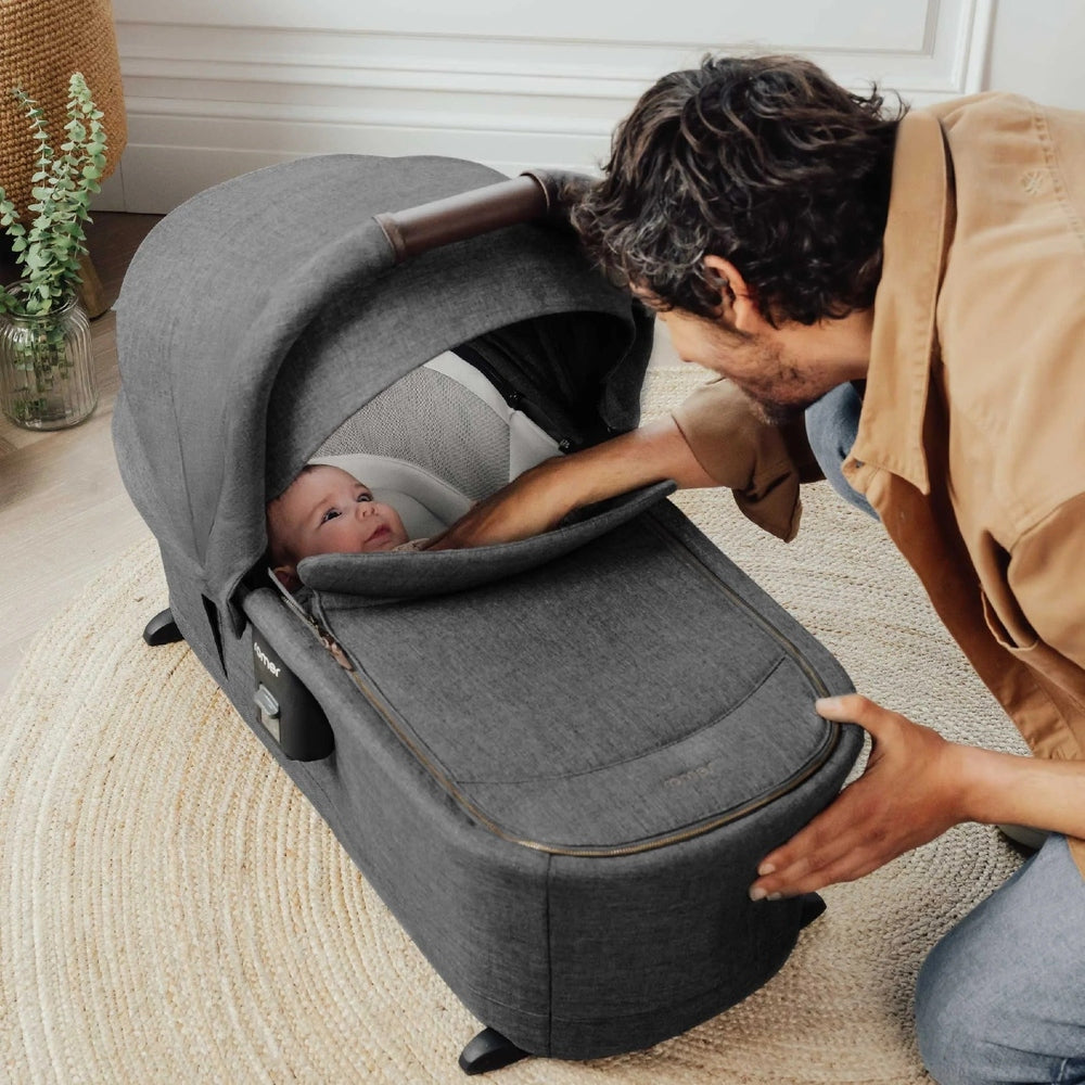 ROMER Sera Bassinet for Tura Stroller in dark gray; parent peeks in on awake baby inside attached bassinet.