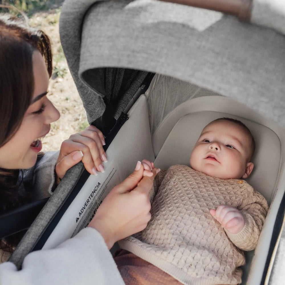 Romer Sera Bassinet for Tura Stroller in beige; mother interacts with baby resting in the cozy stroller bassinet.