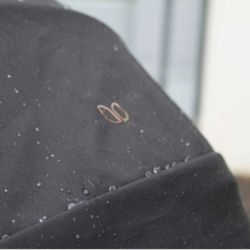 Romer Tura Rain Cover in black, water droplets bead on the surface with ROMER logo visible.