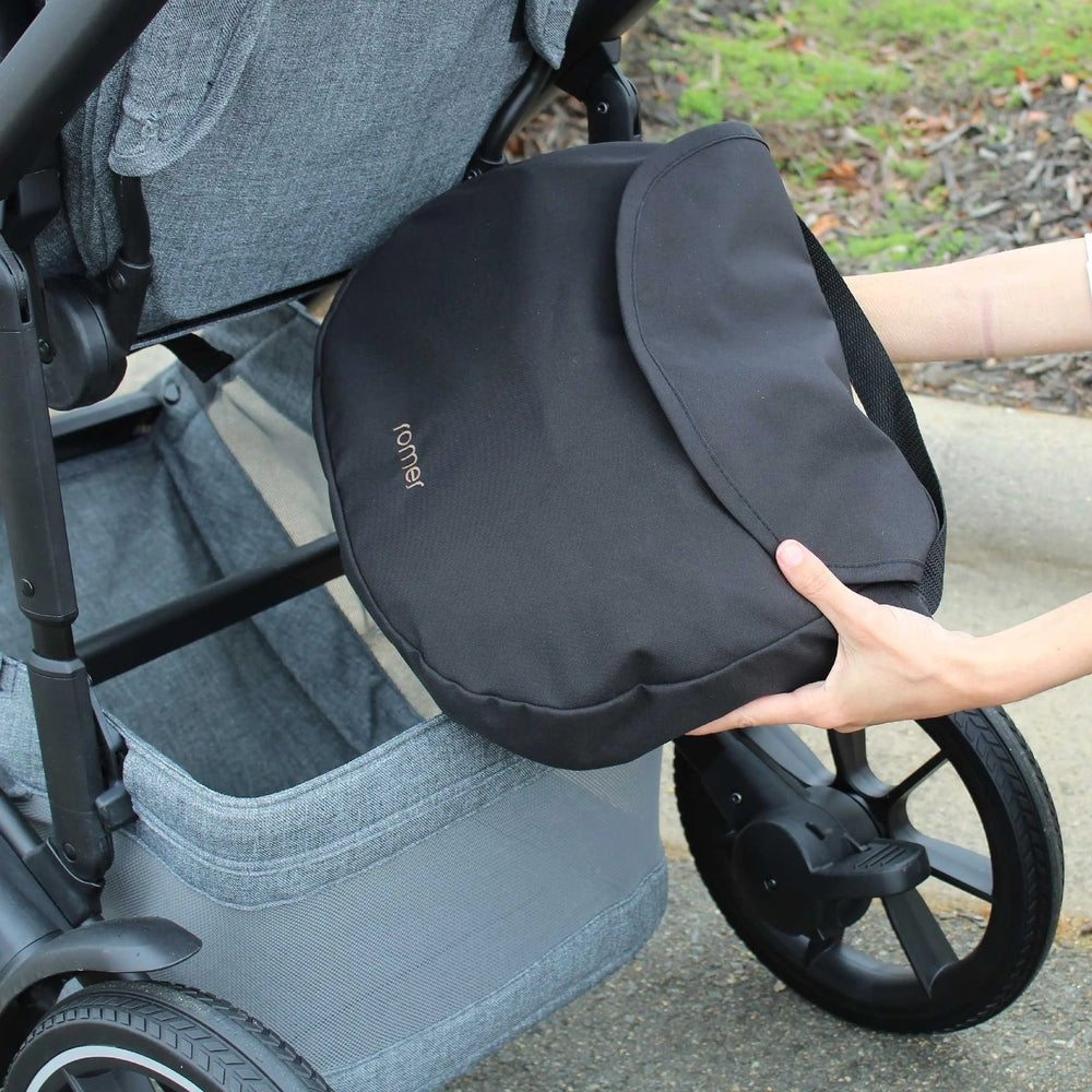 Romer Tura Rain Cover in compact black bag held near a gray stroller, ROMER logo visible.