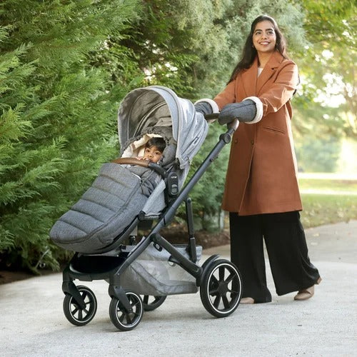 Romer Tura Winter Kit cover and gloves on a baby stroller, as a woman pushes it along a sunny park path.