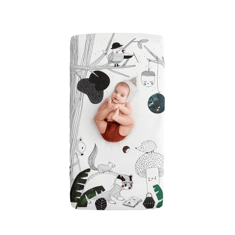 Rookie Humans Woodland Dreams crib sheet in white with illustrated woodland animals; baby lying on sheet.