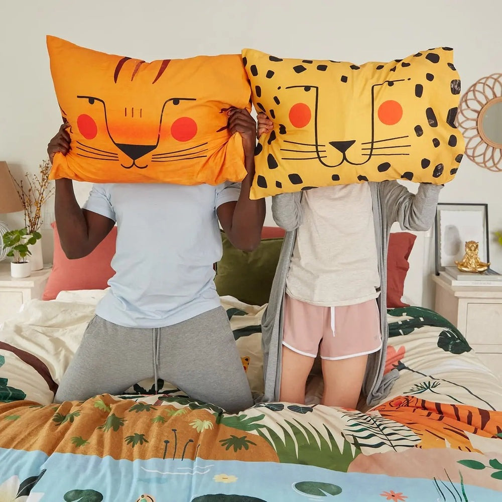 Rookie Humans Kids Bedding Set In The Jungle oversized orange tiger and yellow leopard pillow covers held aloft by two kids.