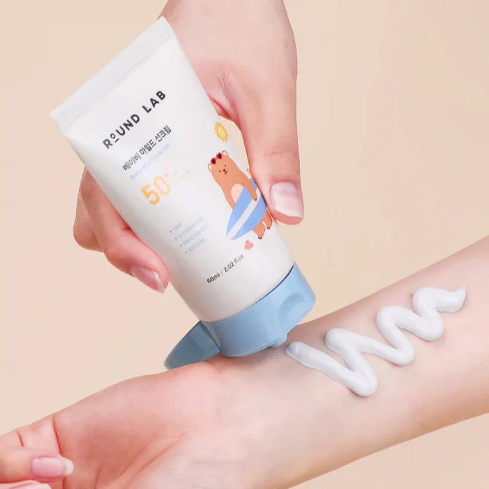 ROUND LAB Baby Mild Sunscreen 60 ml with blue cap being squeezed onto forearm, SPF 50+

