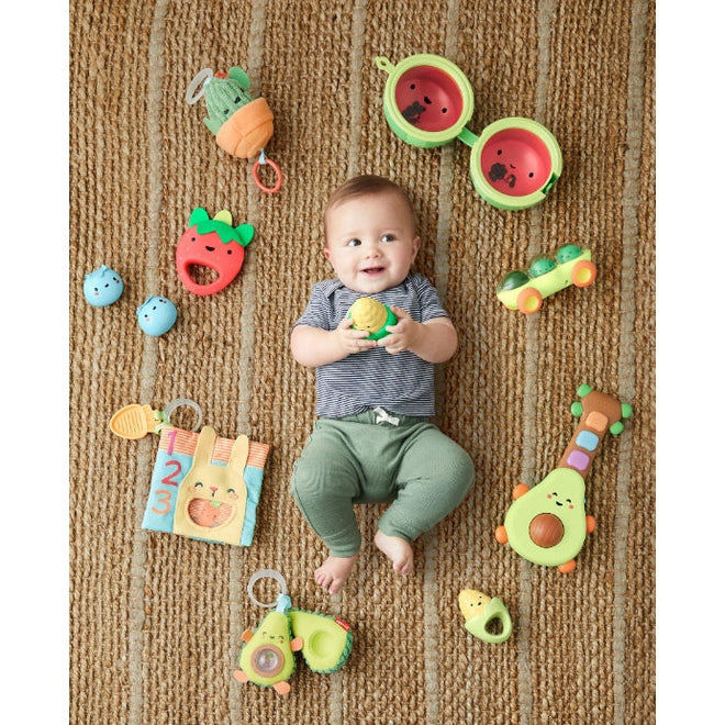 Skip Hop Farmstand Melon Drum baby toy set with colorful farm-themed toys around a smiling baby on a rug