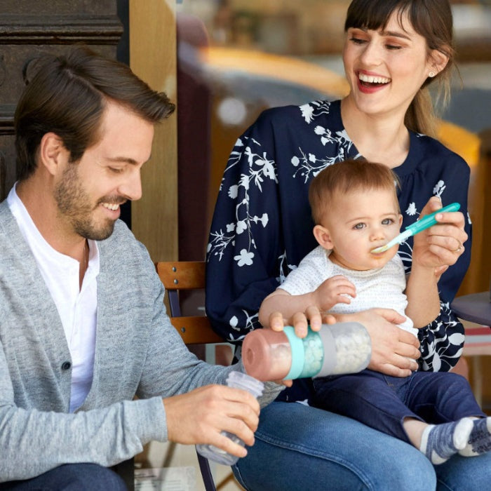 Skip Hop formula-to-food containers set, pink jar with teal lid, held by parents.