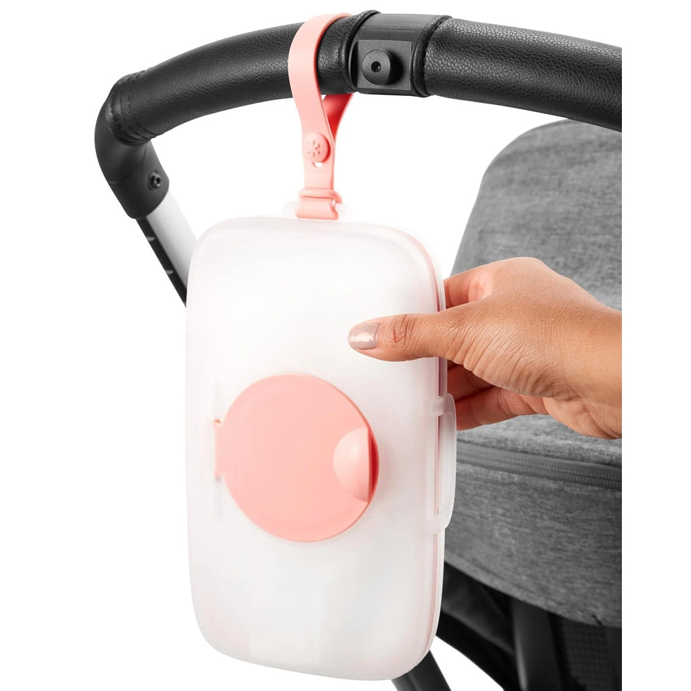 Skip Hop Grab & Go Snug Seal Wipes Case in white with pink lid clipped to a stroller handle by a pink strap.
