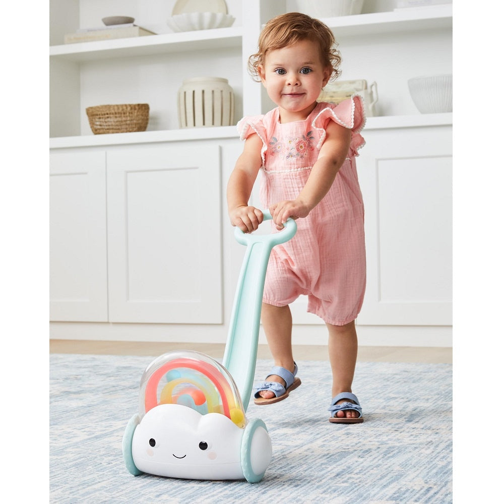 Skip Hop Silver Lining Cloud Rainbow Push Toy with mint handle pushed by toddler in a pink romper