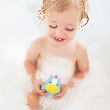 Skip Hop Zoo light-up unicorn bath toy held by a smiling baby in bubbly bath