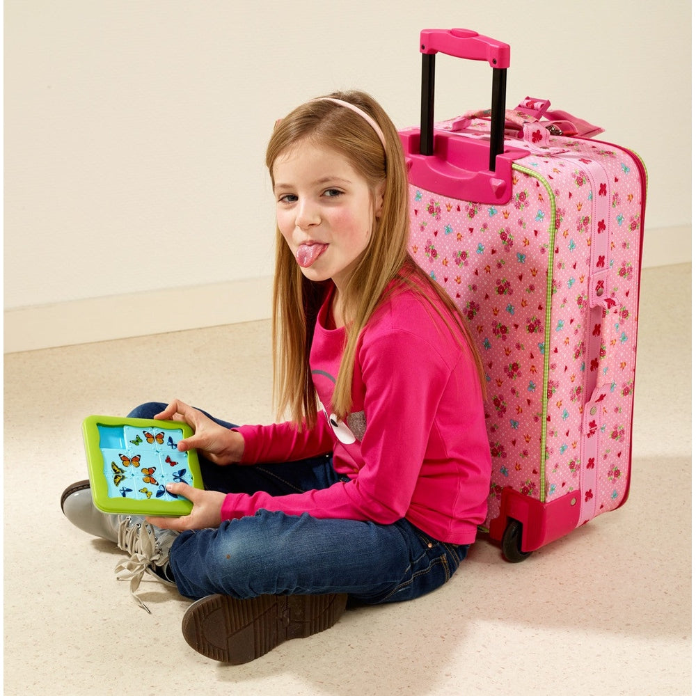 Smart Games Butterflies educational puzzle tablet with green frame; girl sits beside pink butterfly-print suitcase