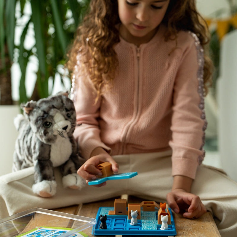 Smart Games Cats & Boxes board game with blue grid and tiny cat pieces; child plays beside a plush cat.