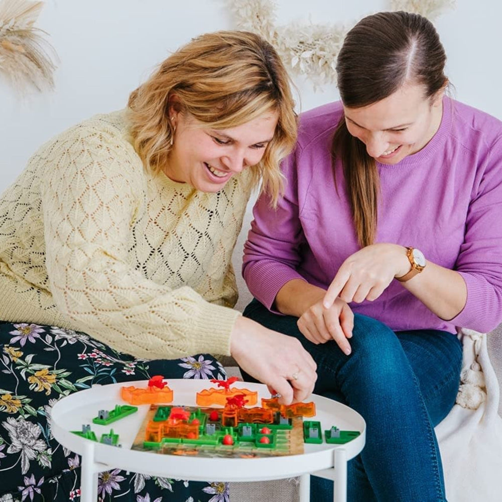 Smart Games Dragon Inferno educational puzzle game played by two adults on a round white table with colorful pieces.